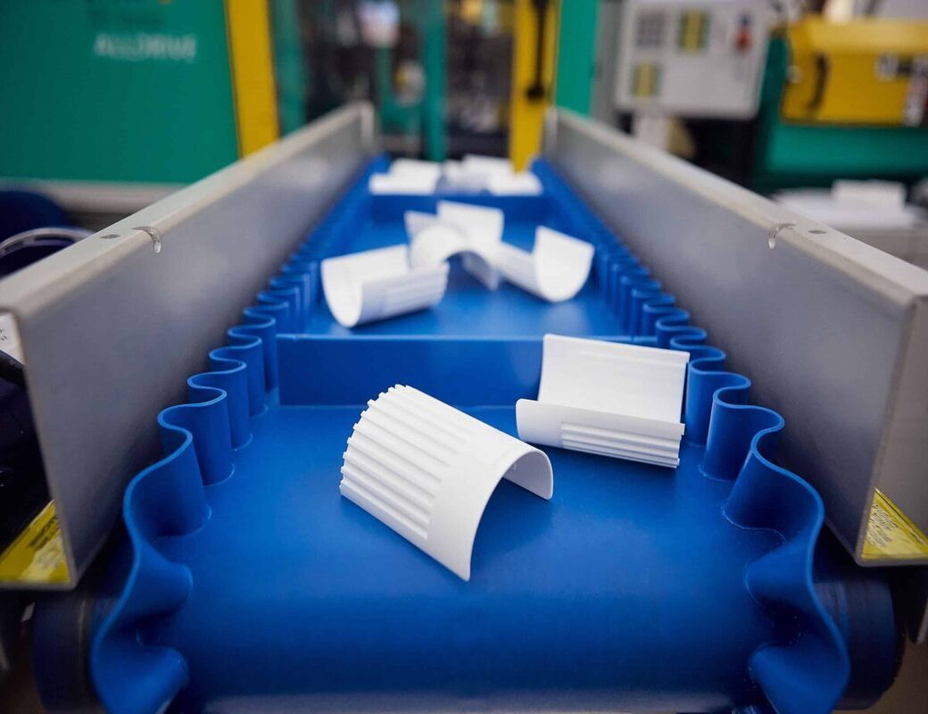 White molded plastic components moving along the production line in a clean molding cell